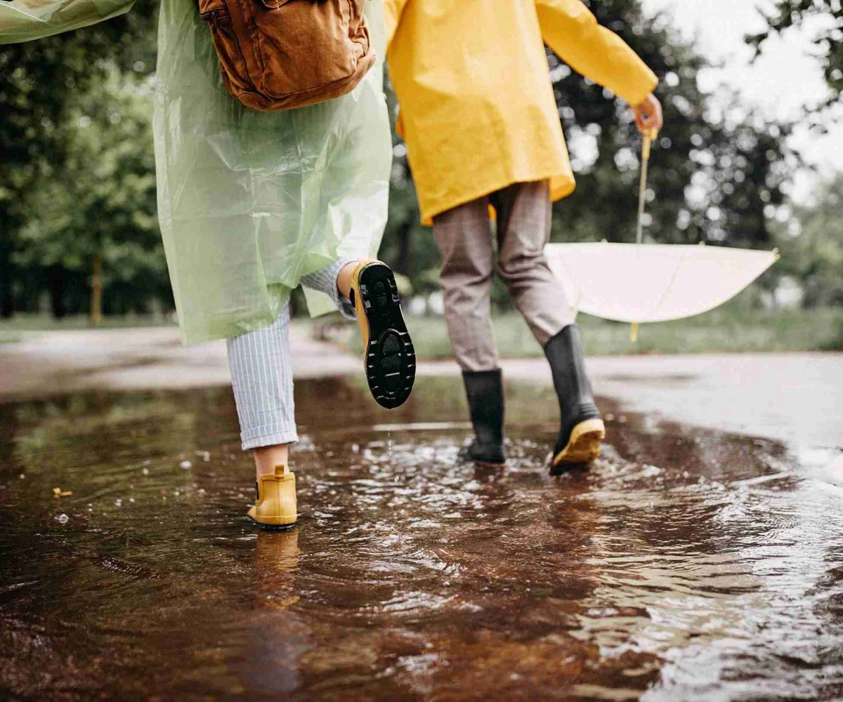 Two People Wearing Rain Gear And Running In Puddles