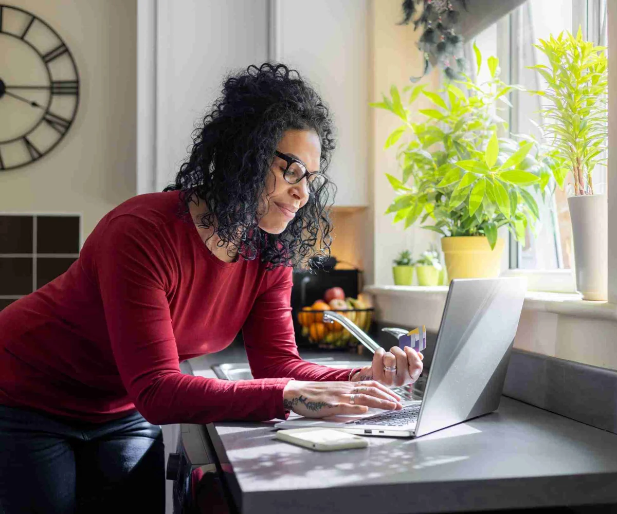 A Woman Leaning On Kitchen Counter Typing Into A Laptop