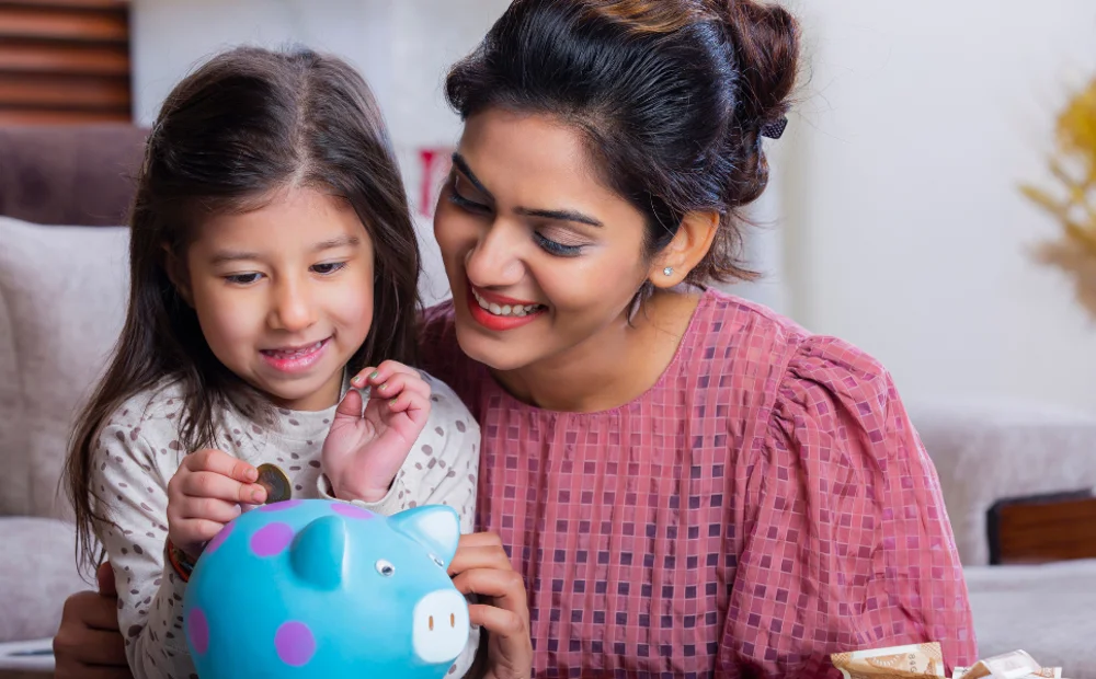 mother and daughter putting coins into blue piggy bank mother and daughter putting coins into blue piggy bank