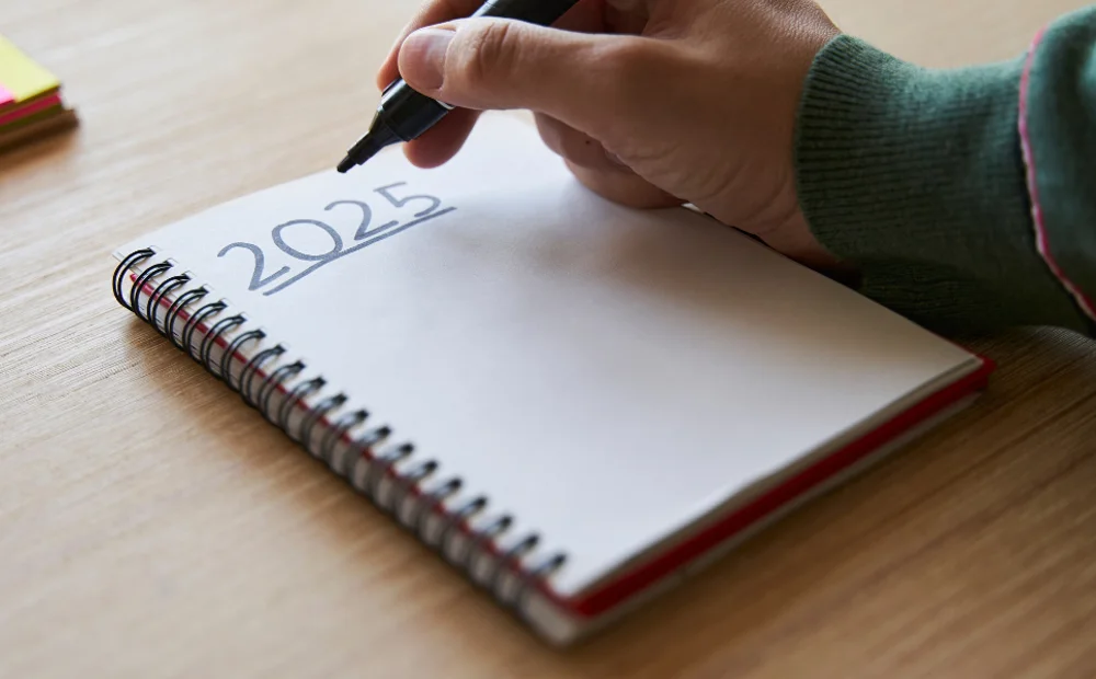person writing '2025' in notebook person writing '2025' in notebook