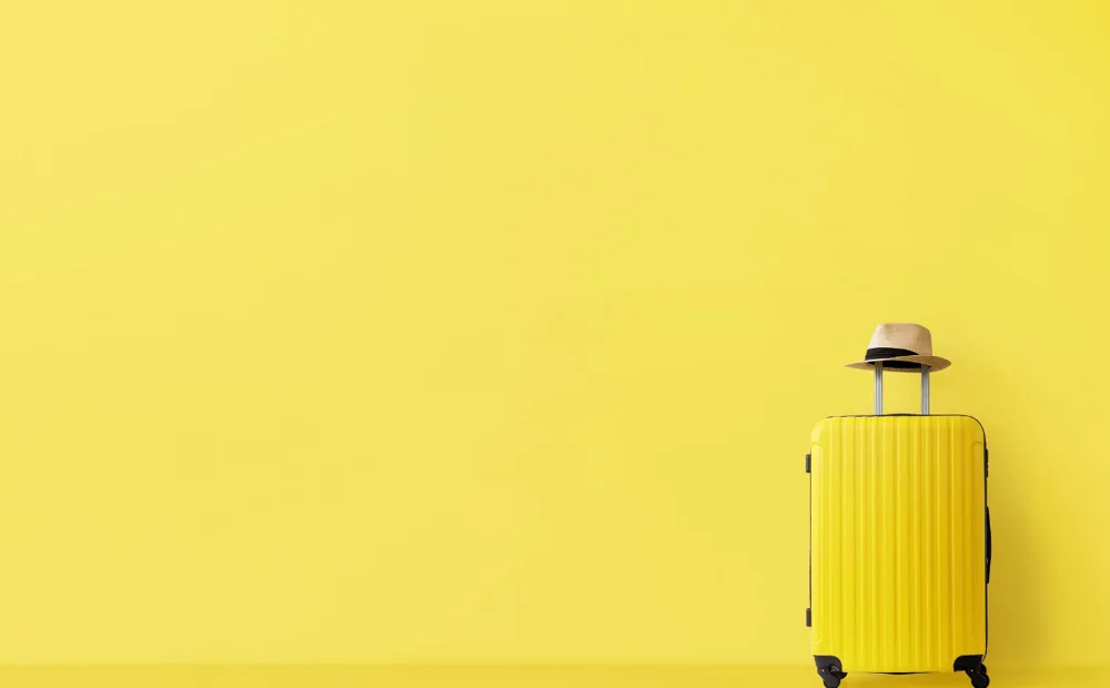 yellow suitcase with fedora on top in front of yellow wall yellow suitcase with fedora on top in front of yellow wall
