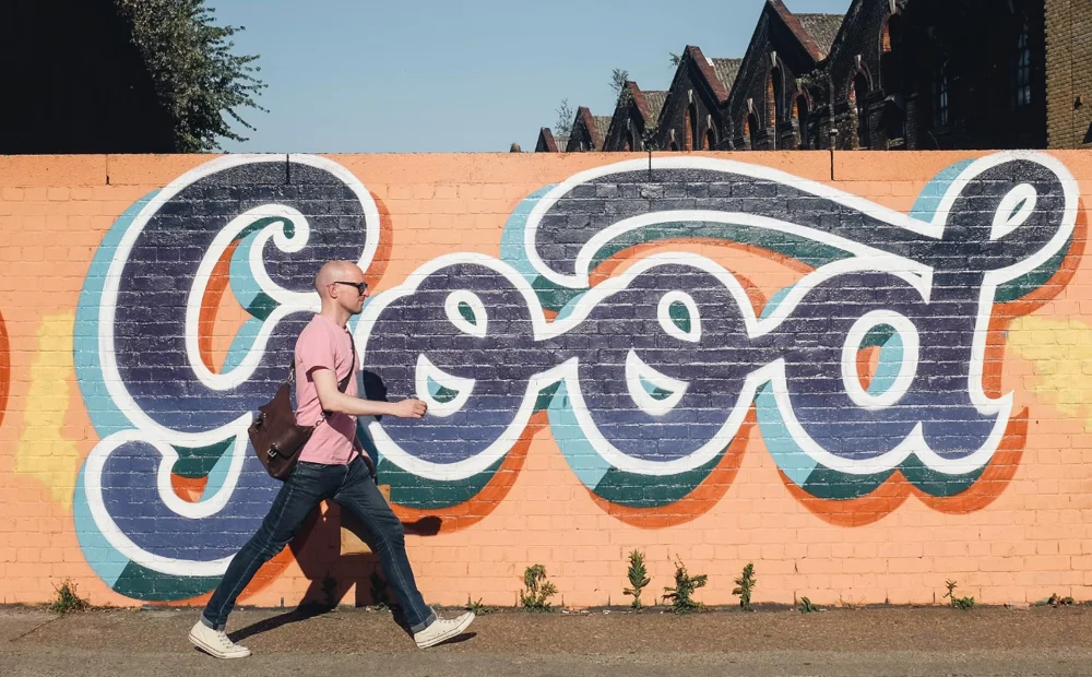 person walking in front of 'good' graffiti person walking in front of 'good' graffiti