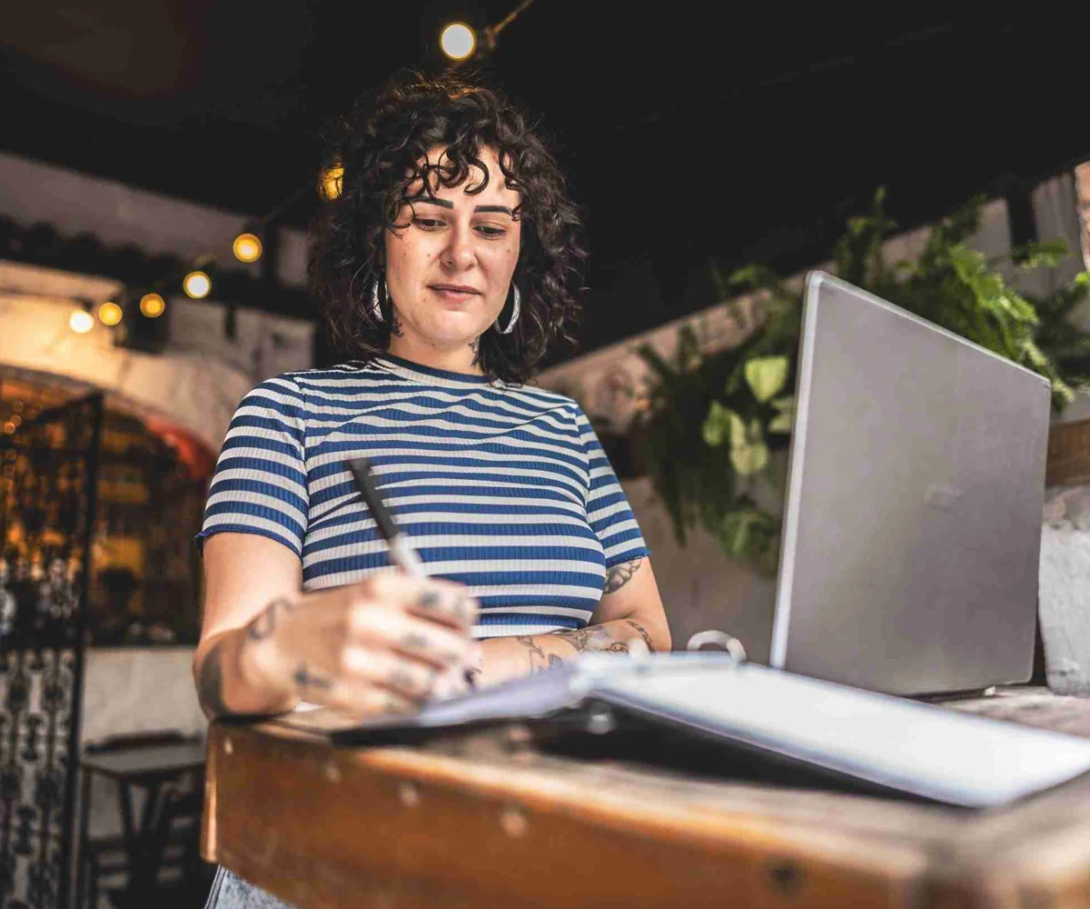 Woman Taking Notes On A Notepad With Her Laptop Open