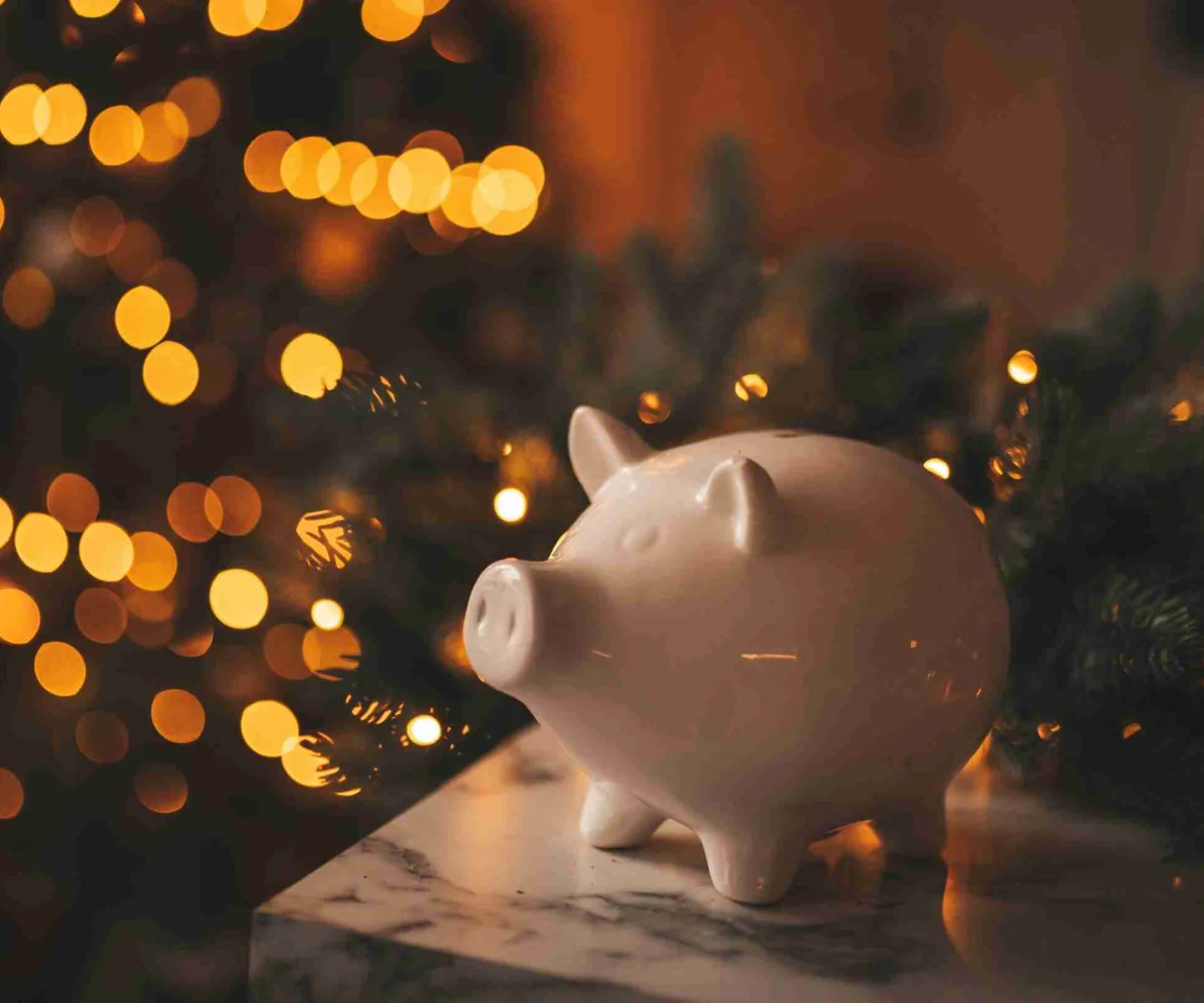 White Piggy Bank In Front Of Lit Up Christmas Tree