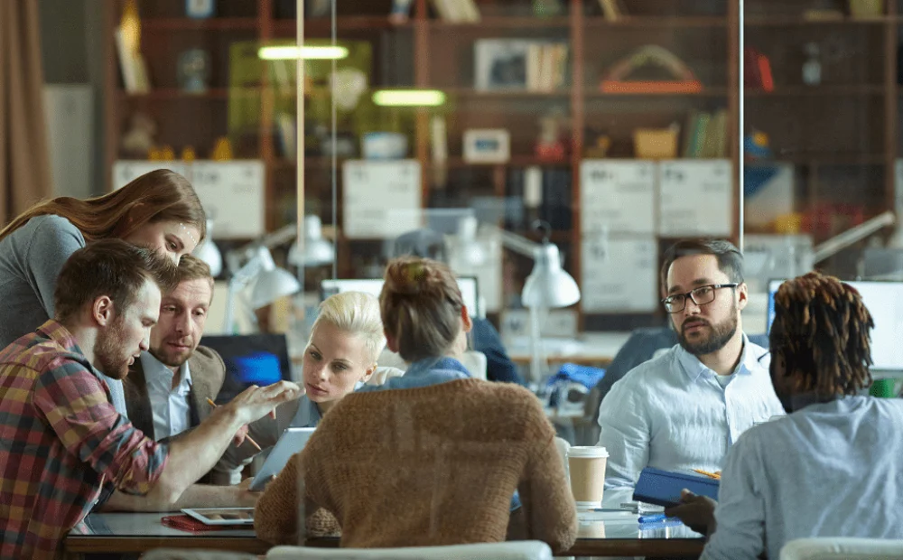 a group of employees sitting at a table in a glass room a group of employees sitting at a table in a glass room