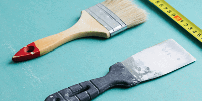Image of a wallpaper scraper , paintbrush and tape measure on a blue background 